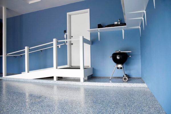 Garage with blue epoxy residential floor coating, a white ramp leading to a door, and a black grill. Floating shelves hold various items.