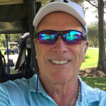 Smiling man in a golf cart on a sunny course, wearing sunglasses reflecting the green landscape. A great day for outdoor residential floor coating work!